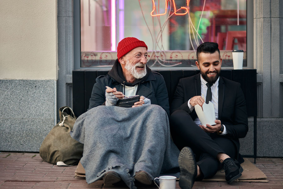 Smiling rich and poor men together sitting on street and eat while speaking